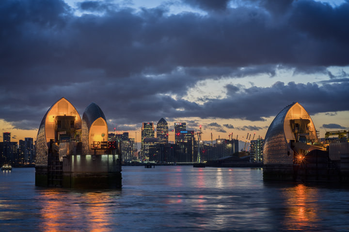 The illuminated Thames barrier and Canary Wharf at dusk